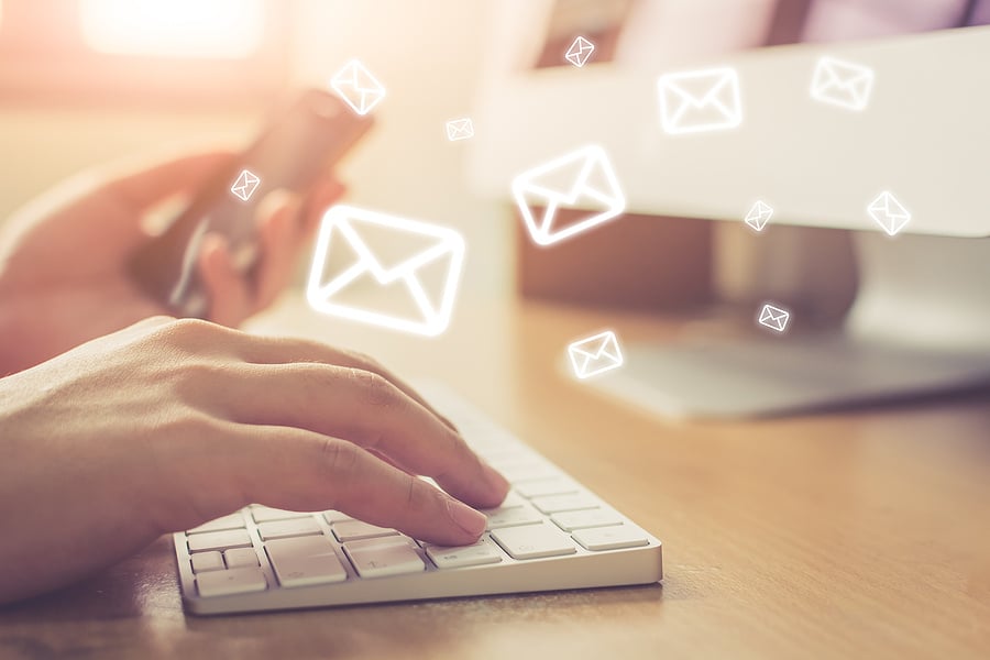 person typing on a keyboard with email icons floating above their hands